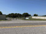 Gravel road with fenced grassy area.