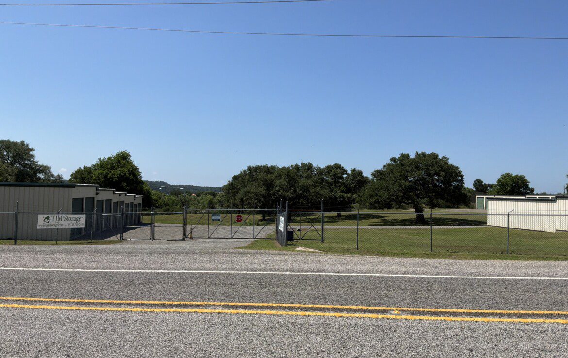 Fenced area with trees and buildings visible.